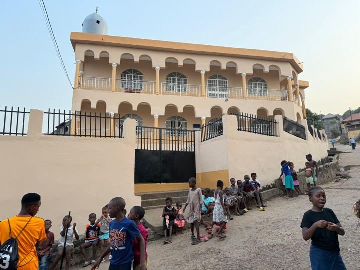 Children sitting along the masjid wall